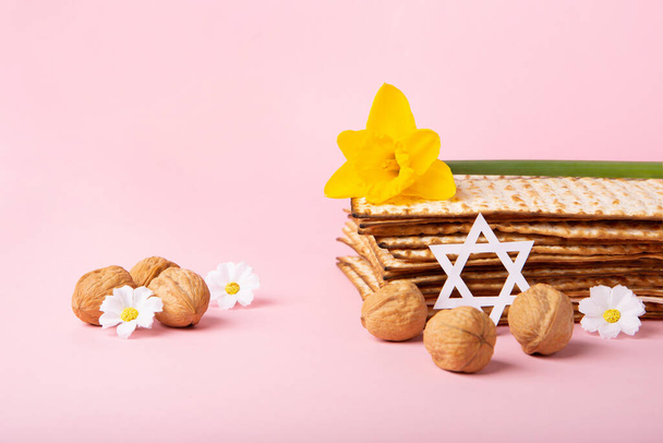 ユダヤ人の休日マツァ、デビッドの星、春の黄色のダフォディ、デイジーの花、ピンクのテーブルの上のクルミと過越グリーティングカードの概念。Seder Pesach春休みの背景、コピースペース. - 写真・画像