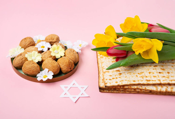 Jewish holiday Passover greeting card concept with matzah, nuts, spring daisy flowers on pink table. Seder Pesach spring holiday background, copy space. - Photo, Image