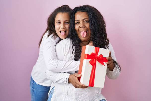 Anne ve küçük kızı ellerinde hediyelerle dillerini çıkarıp komik bir ifadeyle mutlular..  - Fotoğraf, Görsel