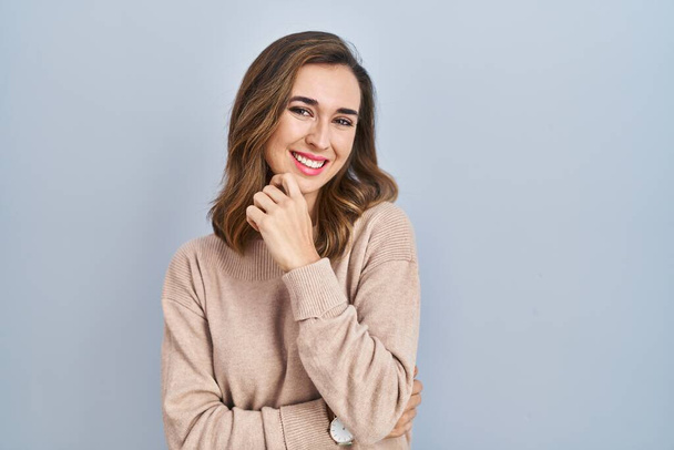 Young woman standing over isolated background looking confident at the camera smiling with crossed arms and hand raised on chin. thinking positive.  - Foto, immagini