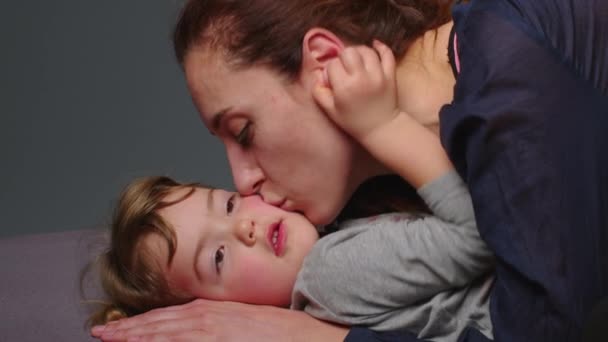 Close-up shot van jonge moeder is spelen en kussen met haar kleine meisje in een ochtend op grijze achtergrond. Concept van kinderen, baby, ouderschap, kindertijd, leven, moederschap, moederschap. - Video