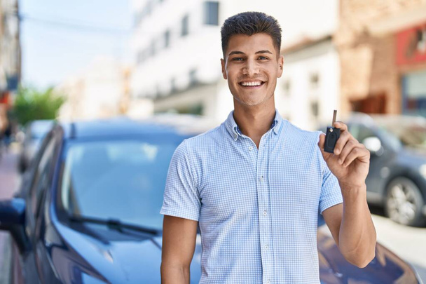 Young hispanic man holding car key looking positive and happy standing and smiling with a confident smile showing teeth  - Foto, imagen