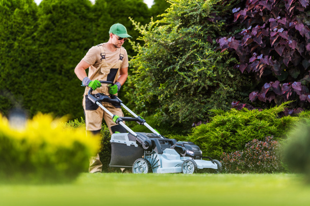 Professional Gardener Mowing the Lawn with Cordless Battery Powered Electric Mower. Residential Garden Maintenance Theme. - Fotografie, Obrázek