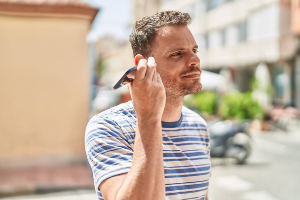 Молодий іспаномовний чоловік слухає аудіоповідомлення по смартфону на вулиці
 - Фото, зображення