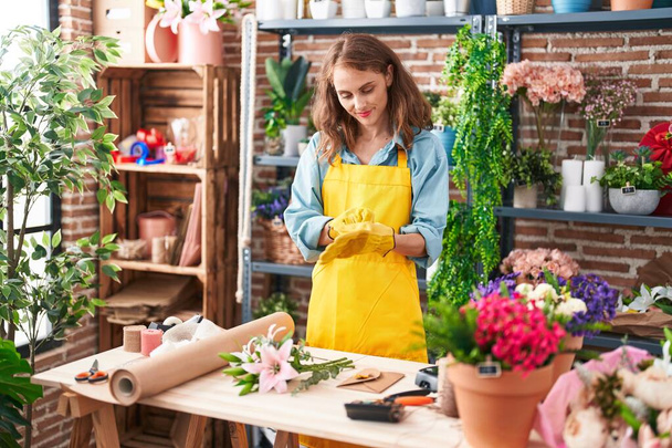 Young beautiful hispanic woman florist smiling confident wearing gloves at florist - Photo, Image