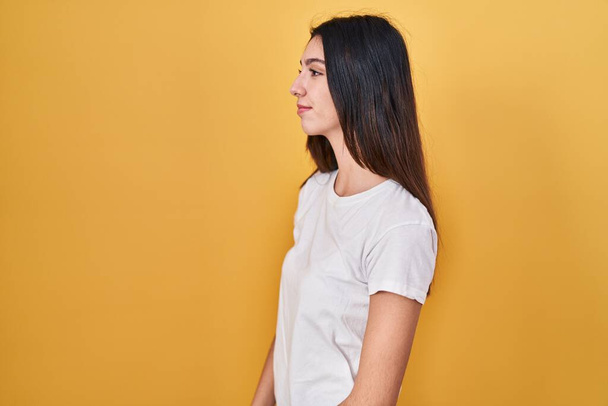 Young beautiful woman standing over yellow background looking to side, relax profile pose with natural face and confident smile.  - Foto, afbeelding