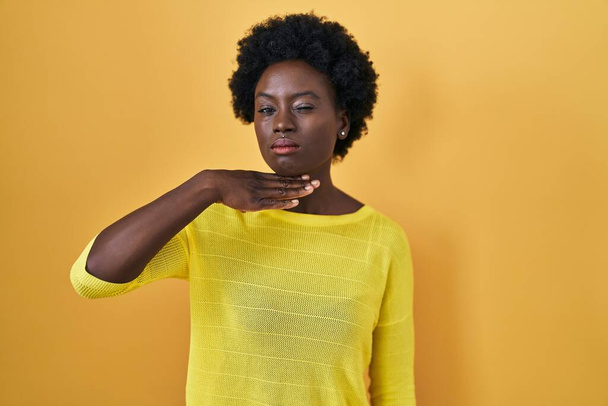 Африканская молодая женщина, стоящая над желтой студией, перерезает горло рукой, как нож, угрожает агрессией яростным насилием  - Фото, изображение