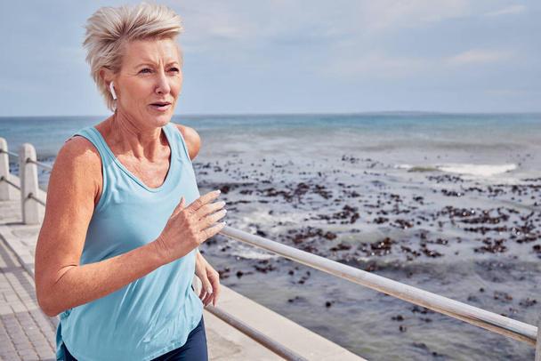Idős nő, testmozgás és futás a tengerparti sétányon, égi mockup vagy az egészség, wellness és edzés energiája. Időskorú nő, fülhallgató és fitnesz a sport óceánjában, kardio futó és erős gondolkodásmód. - Fotó, kép