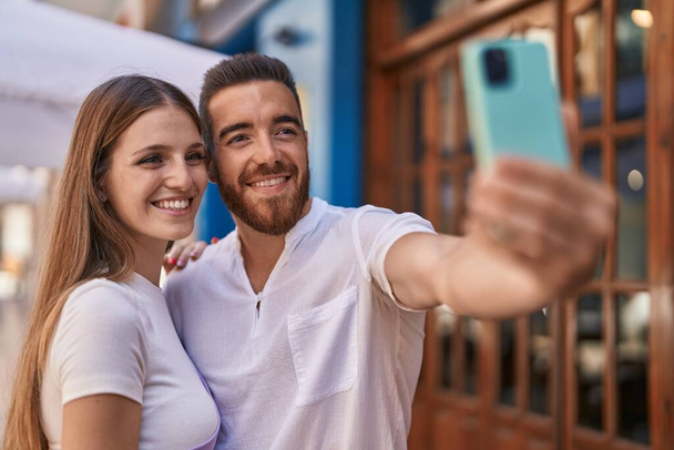 Kadın ve erkek, güler yüzlü, özgüvenli bir şekilde sokakta akıllı telefondan selfie çekiyorlar. - Fotoğraf, Görsel