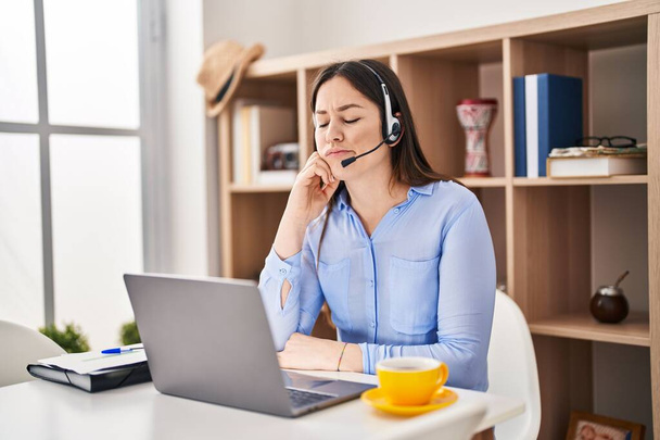 Young brunette woman wearing call center agent headset serious face thinking about question with hand on chin, thoughtful about confusing idea  - Photo, Image