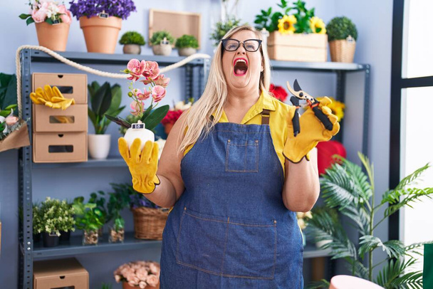 Caucásico más tamaño mujer trabajando en floristería enojado y loco gritando frustrado y furioso, gritando con ira mirando hacia arriba.  - Foto, imagen