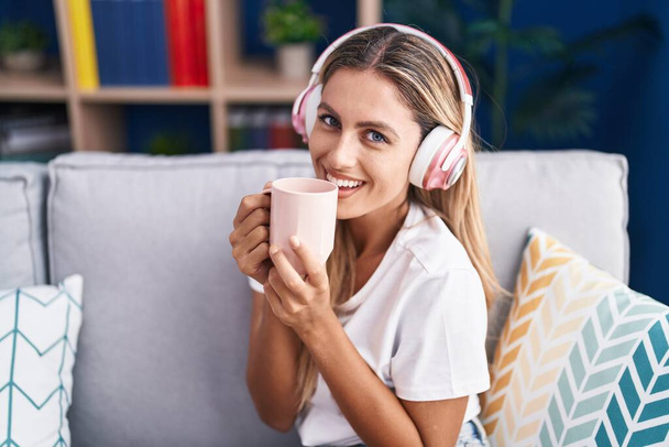 Mujer rubia joven escuchando música tomando café en casa - Foto, Imagen
