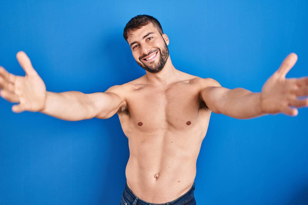 Handsome hispanic man standing shirtless looking at the camera smiling with open arms for hug. cheerful expression embracing happiness.  - Zdjęcie, obraz