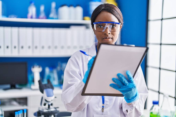 Young african american woman scientist writing on document at laboratory - Foto, Bild