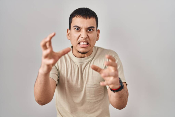 Young arab man wearing casual t shirt shouting frustrated with rage, hands trying to strangle, yelling mad  - Foto, imagen