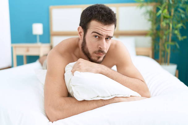 Young hispanic man lying on bed with relaxed expression at bedroom - 写真・画像