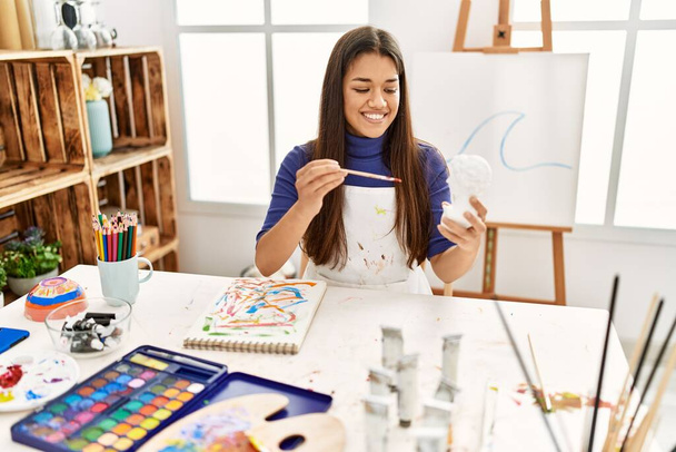 Молодая латиноамериканка улыбается уверенной картине бюст скульптуры в художественной студии - Фото, изображение