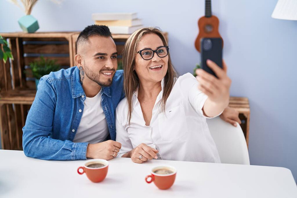 Man and woman mother and son drinking coffee make selfie by smartphone at home - Fotó, kép