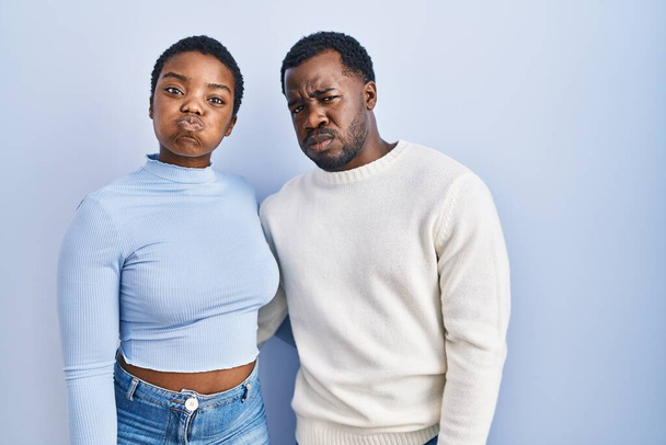 Giovane coppia afro-americana in piedi sopra sfondo blu sbuffare guance con la faccia divertente. bocca gonfia d'aria, espressione folle.  - Foto, immagini