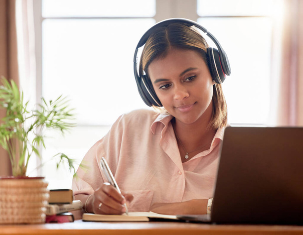 Woman, student with laptop and headphones, writing notes in notebook, education and elearning with study notes. Mexican female, internet with wifi and tech, online class with webinar and studying. - Fotó, kép