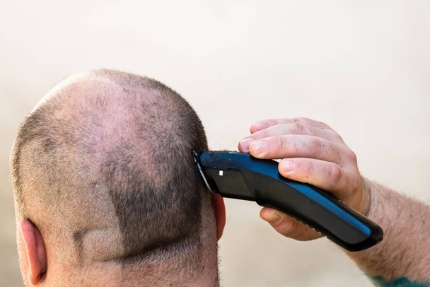 Afeitarse o cortarse el cabello con un cortador de pelo o una máquina de afeitar eléctrica - Foto, imagen