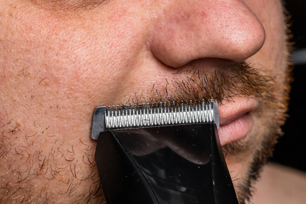 Mann rasiert oder schneidet sich den Bart mit Haarschneidemaschine - Foto, Bild