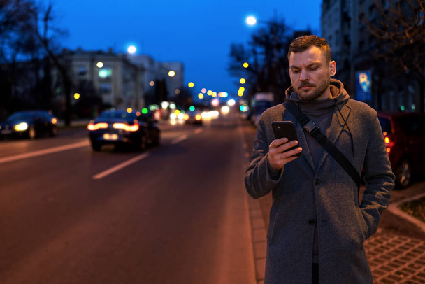 Hombre en la ciudad nocturna usando la aplicación de servicio de granizo de paseo en su teléfono móvil. - Foto, imagen