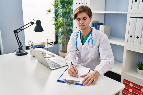Young caucasian man doctor writing medical report at clinic - Foto, Bild