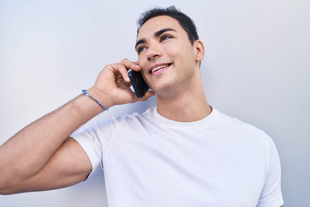 Genç, İspanyol asıllı, kendine güvenen, izole beyaz arka planda akıllı telefondan konuşan adam. - Fotoğraf, Görsel
