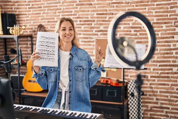 Fiatal kaukázusi nő csinál online zenei bemutató zenei lap mosolyog egy ötlettel vagy kérdéssel ujjal mutogató boldog arc, első számú  - Fotó, kép