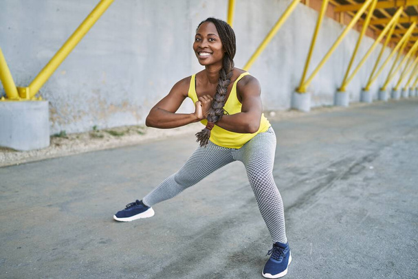 Αφροαμερικανή γυναίκα που φοράει αθλητικά που τεντώνει το πόδι της στο δρόμο - Φωτογραφία, εικόνα