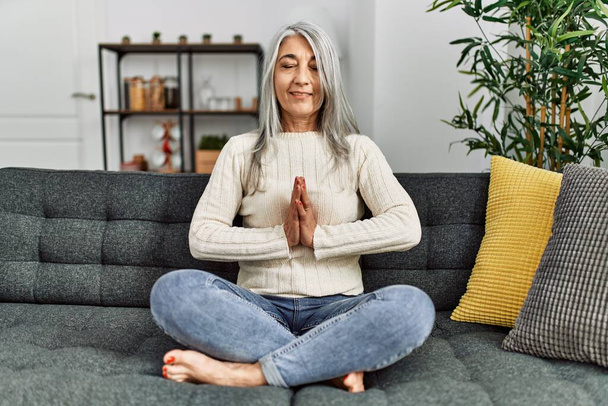 Middelbare leeftijd grijs-harige vrouw glimlachend zelfverzekerd doen yoga oefening thuis - Foto, afbeelding