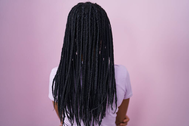 African american woman with braids standing over pink background standing backwards looking away with crossed arms  - 写真・画像