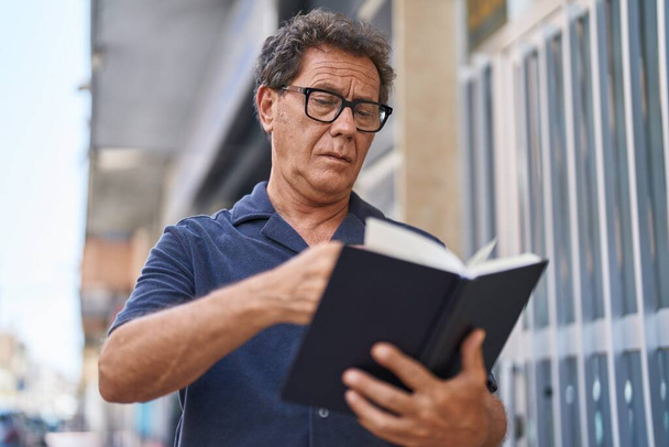 Muž středního věku čtení knihy s uvolněným výrazem na ulici - Fotografie, Obrázek