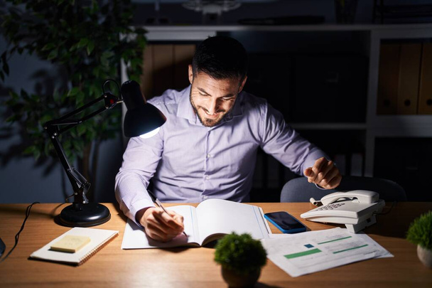 Jovem hispânico homem empresário escrevendo no notebook trabalhando horas extras no escritório - Foto, Imagem