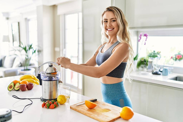 Молодая женщина улыбается уверенно, используя блендер на кухне - Фото, изображение