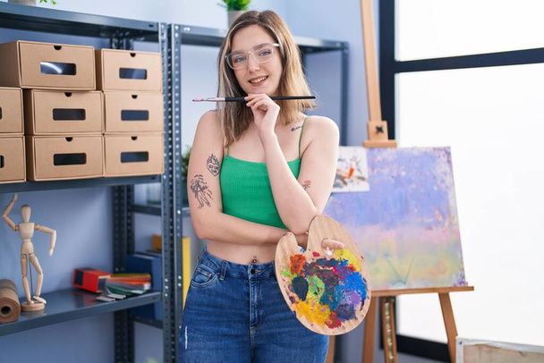 Young woman artist holding paintbrush and palette at art studio - Foto, immagini