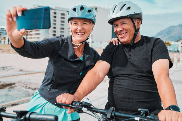 Ποδηλασία, χαμόγελο και τηλέφωνο με ηλικιωμένο ζευγάρι και selfie για social media, προπόνηση και προπόνηση υγείας. Ευεξία, internet και blog με ηλικιωμένους άνδρες και γυναίκες σε ποδήλατο για το καλοκαίρι, την άσκηση και τα ταξίδια. - Φωτογραφία, εικόνα
