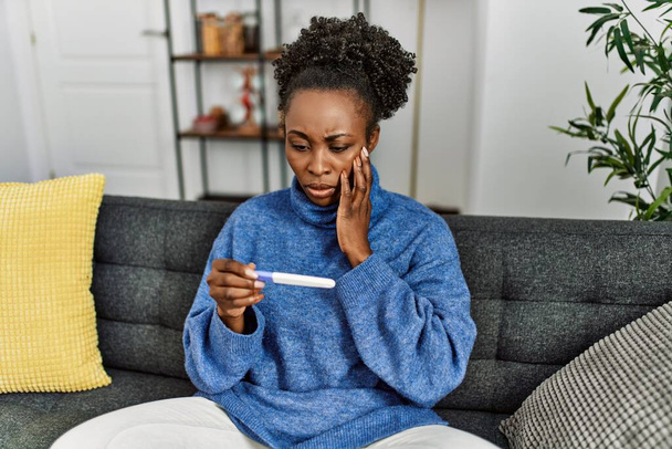 African american woman holding pregnancy test with worried expression at home - Foto, imagen