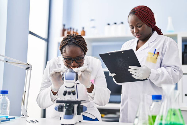 Африканские американские женщины-ученые используют микроскоп для написания документов в лаборатории - Фото, изображение