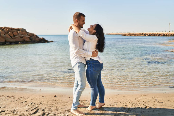Homem e mulher casal sorrindo feliz abraçando uns aos outros em pé à beira-mar - Foto, Imagem