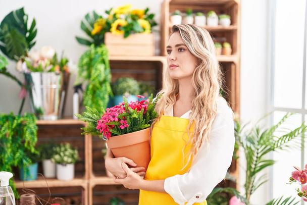 Young blonde woman florist holding plant at florist - Foto, Bild