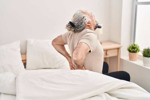 Middle age grey-haired man suffering for back injury sitting on bed at bedroom - Zdjęcie, obraz