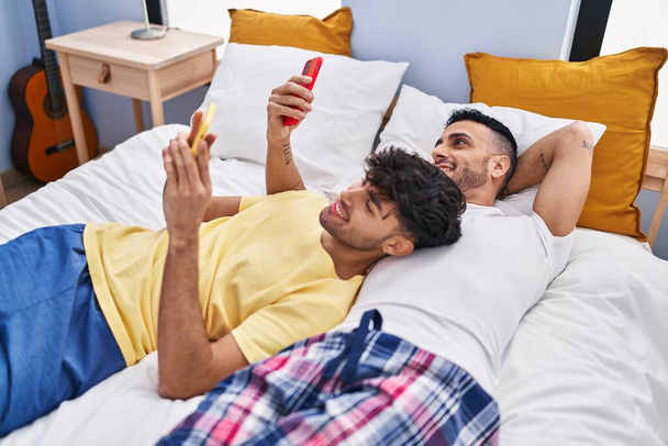 Dos hombre pareja usando teléfono inteligente acostado en la cama en el dormitorio - Foto, Imagen