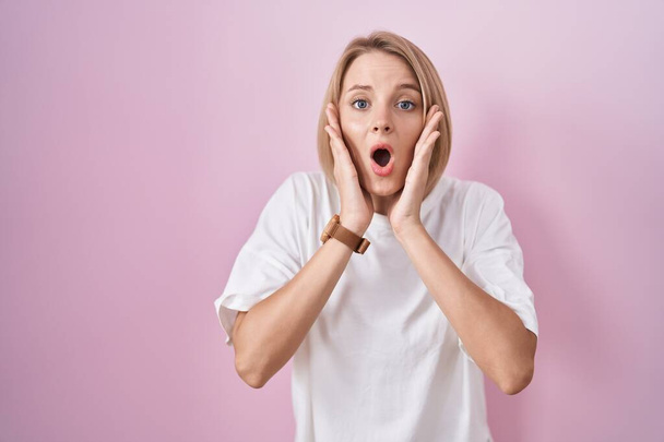 Young caucasian woman standing over pink background afraid and shocked, surprise and amazed expression with hands on face  - Foto, immagini