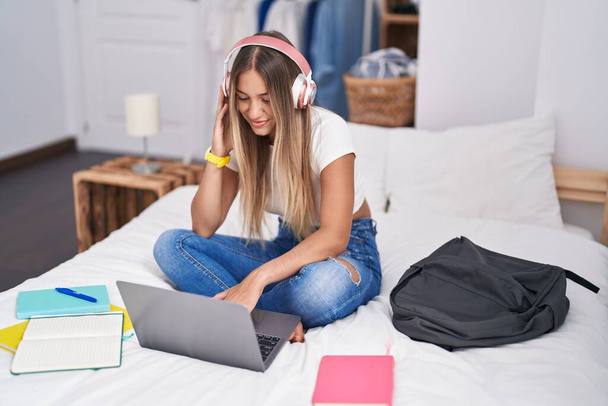 Young beautiful hispanic woman student sitting on bed listening to music at bedroom - Foto, Imagem