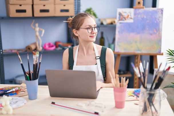 Молода біла жінка художник посміхається впевнено використовуючи ноутбук в художній студії
 - Фото, зображення