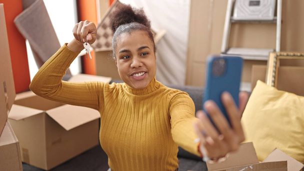 Jeune femme afro-américaine souriante confiante tenant la clé faisant appel vidéo à la nouvelle maison - Photo, image