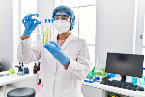 Young latin woman wearing scientist uniform holding test tube at laboratory - Foto, Imagem