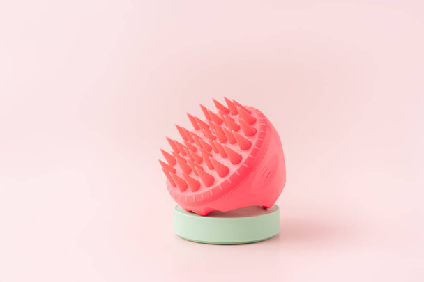 Pink color scalp massager on green stand against pink background. - 写真・画像